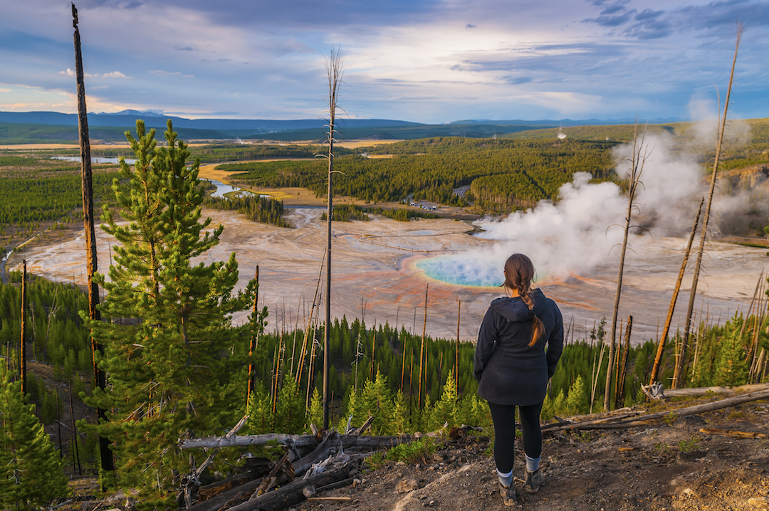 A hiker stands on an overlook, watching the steam rise from the Grand Prismatic Springs in Yellowstone National Park.