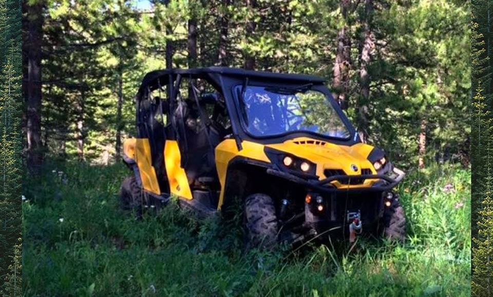 A yellow utility terrain vehicle sits amongst trees in the middle of a forest in Jackson Hole, WY